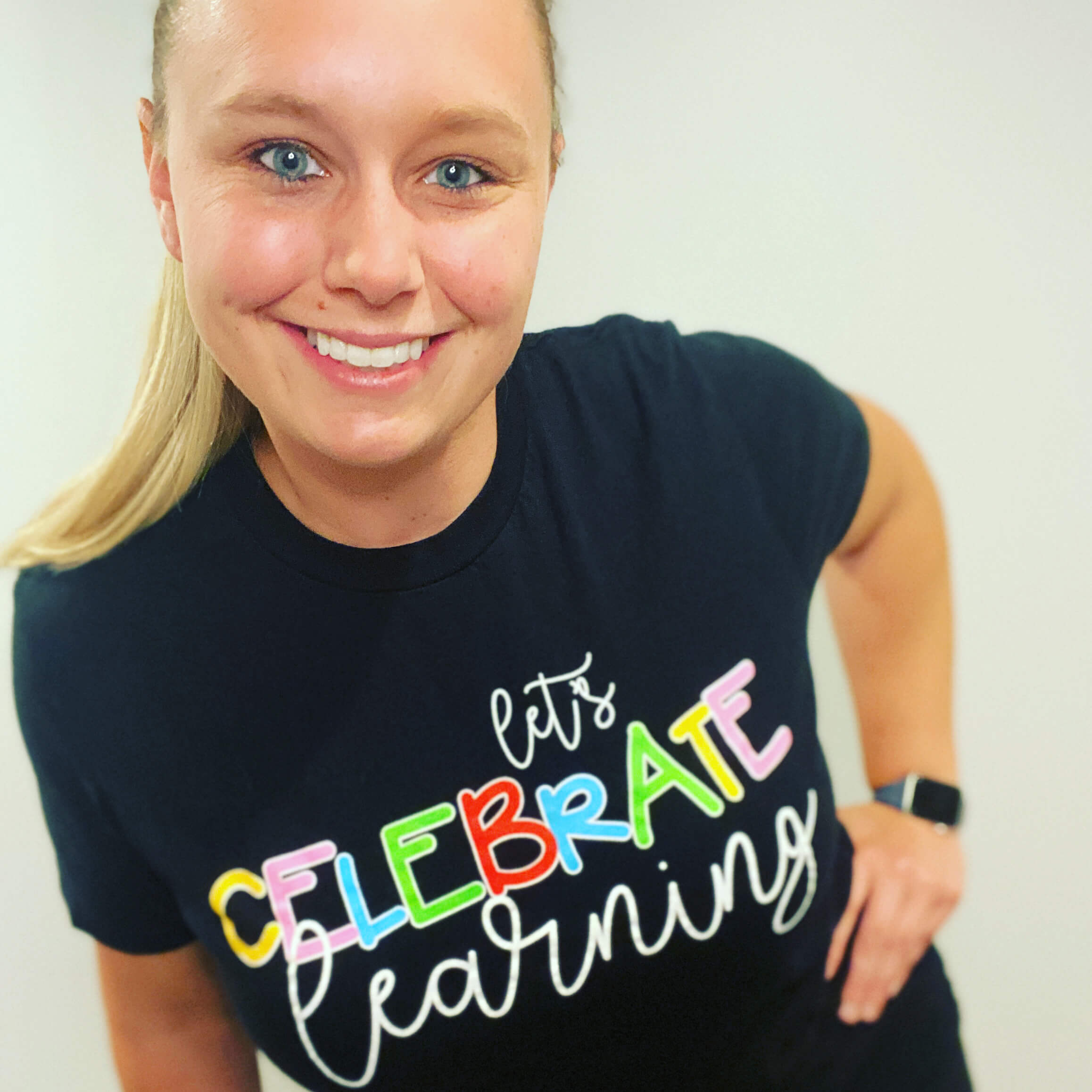 Heather smiling with a black shirt that says Let's Celebrate Learning and her left hand on her hip.